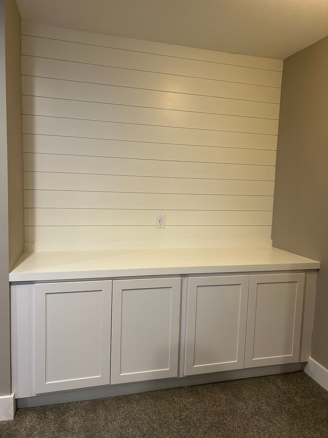 White shiplap wall with modern cabinetry and countertop in a minimalist interior.