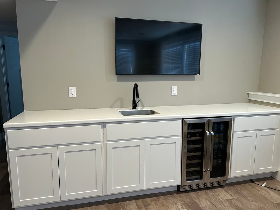 Modern kitchen with gray cabinetry, sink, and a wine cooler under a wall-mounted TV.