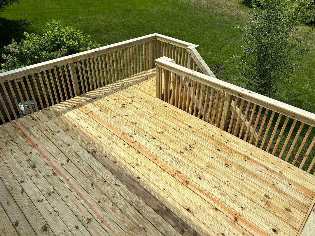 Newly built wooden deck with railings overlooking a green lawn.