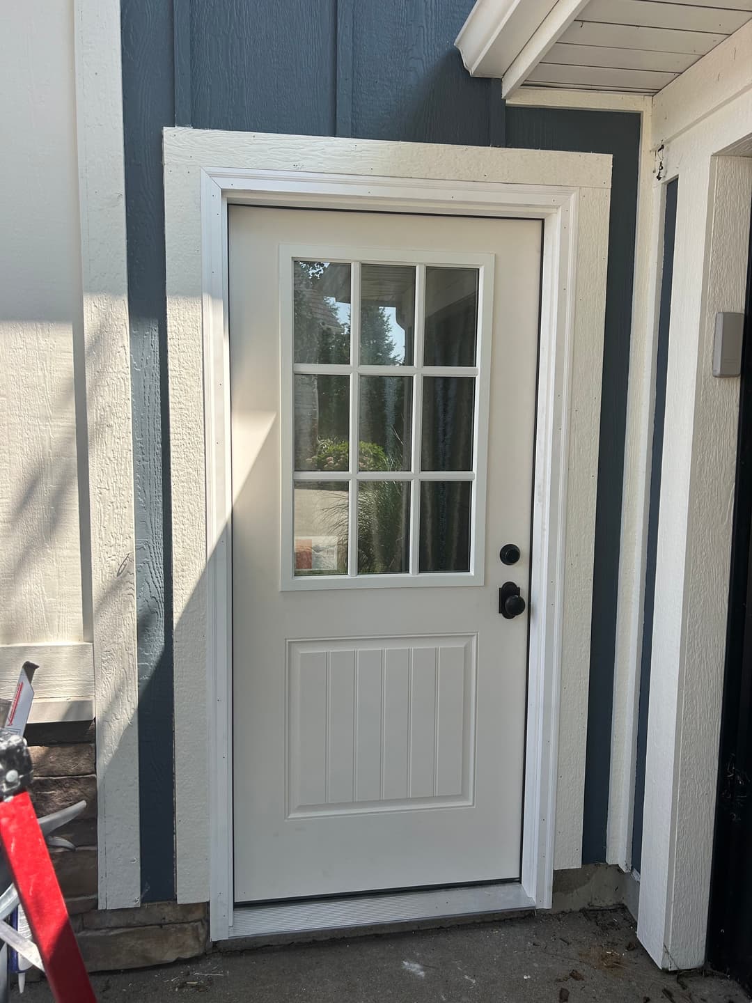 Exterior view of a white door with glass panel, surrounded by blue and white siding.