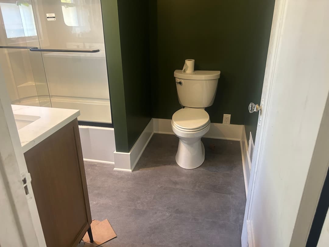 Modern bathroom with green walls, white toilet, and shower area featuring minimalist design.