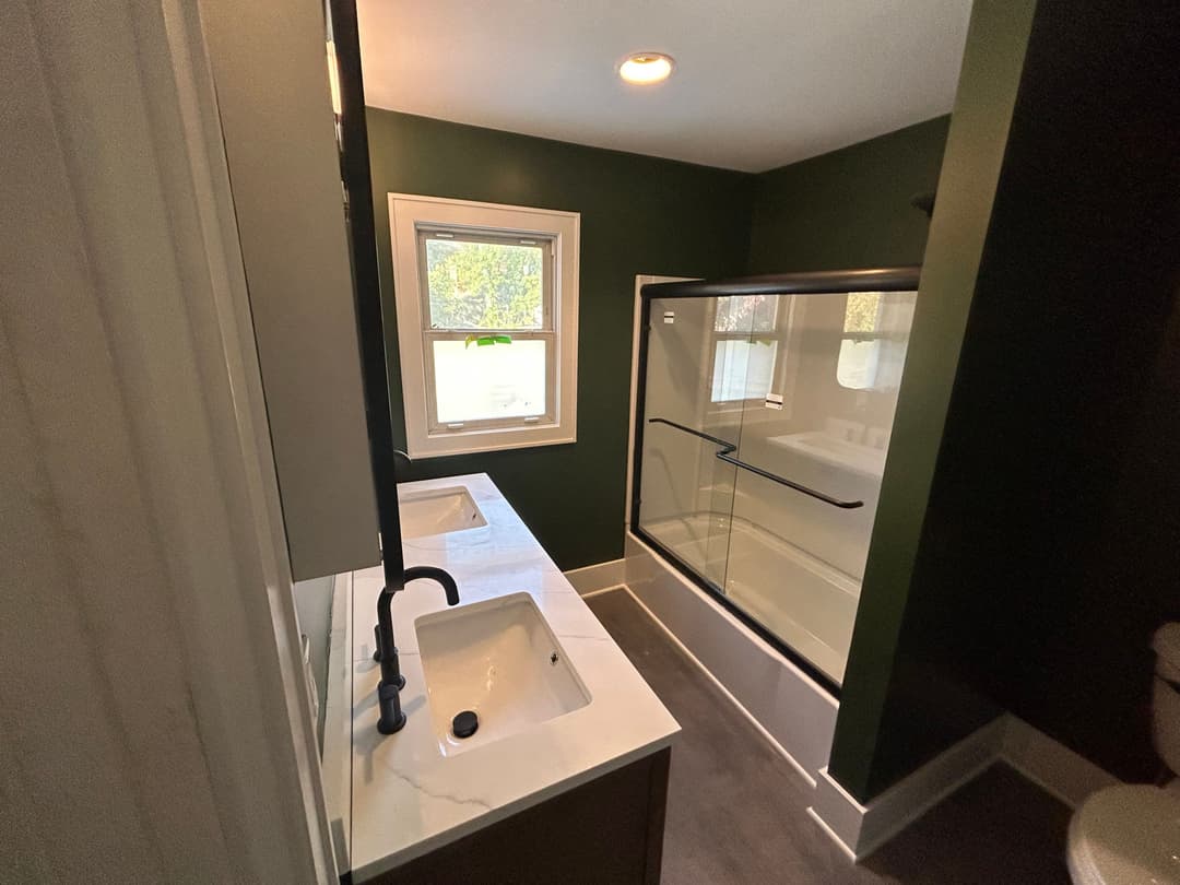 Modern bathroom with green walls, double sinks, and a glass shower enclosure.