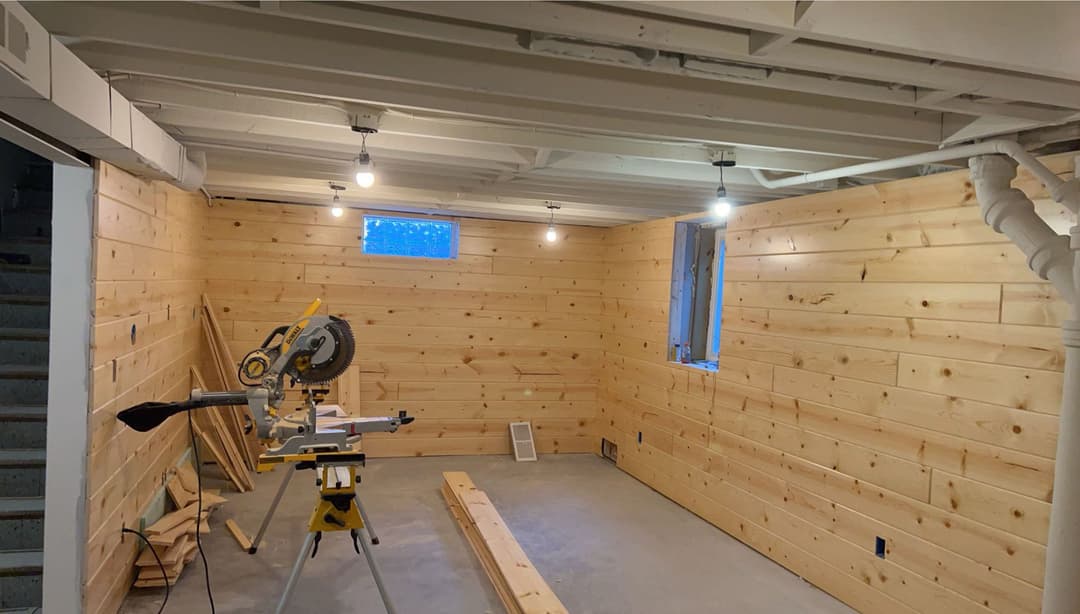 Wood-paneled basement workshop with miter saw and tools, well-lit with overhead lights.