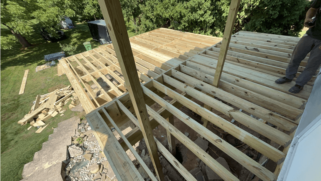 Deck construction in progress with wooden beams and framework visible outdoors.