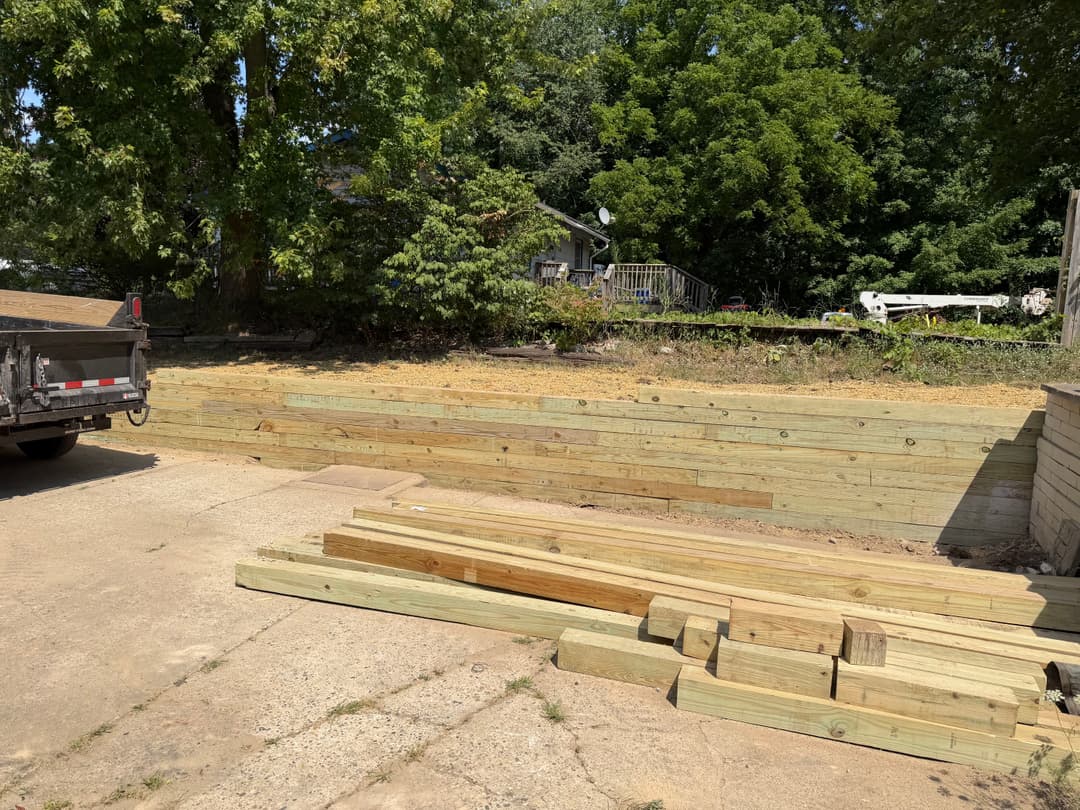 Wooden materials stacked near a recently built retaining wall in a landscaped area.