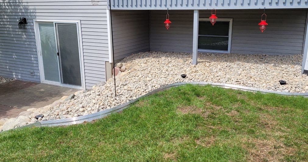 Rock landscape with a curved border, grass area, and three red hummingbird feeders.
