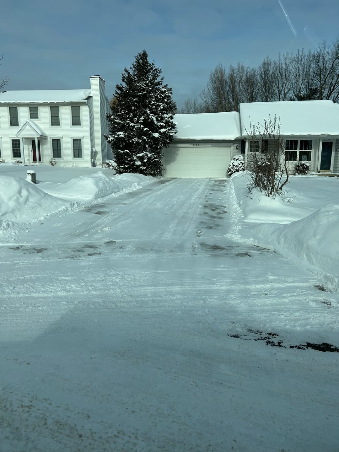 Snow-covered residential driveway with houses and trees in a winter landscape.