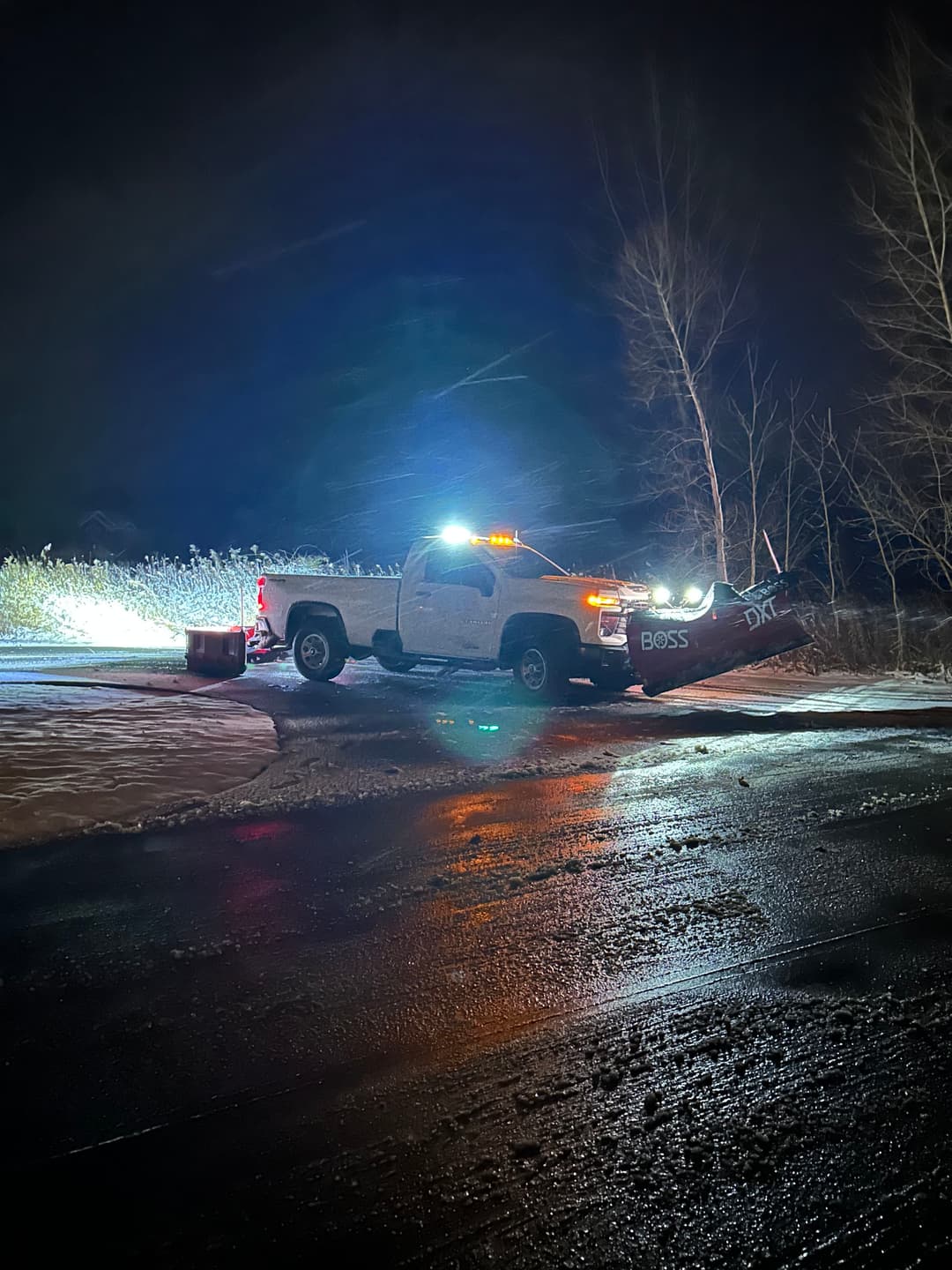 Snow plow truck with lights clearing a snowy road at night.