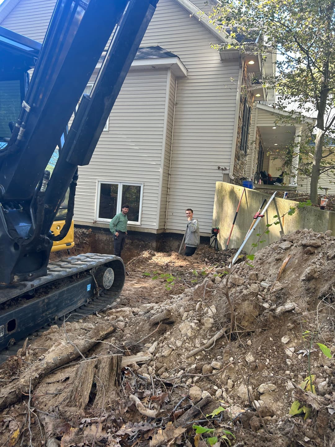 Construction workers beside a house undergoing excavation and foundation work.
