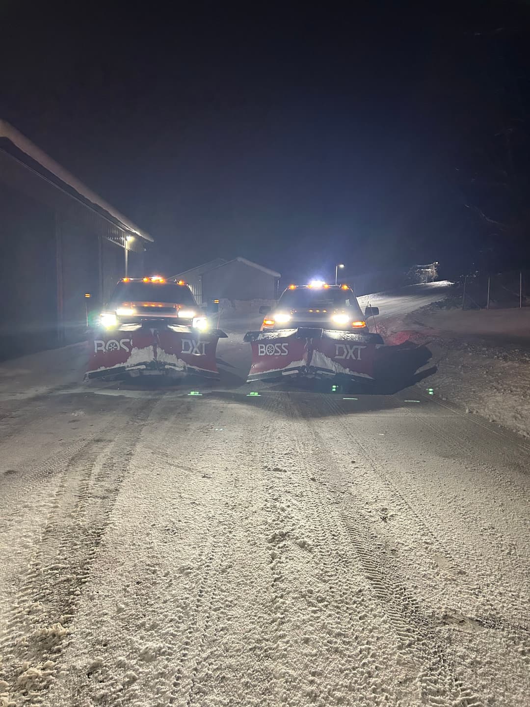 Two snow plows with lights at night clearing a snowy road.