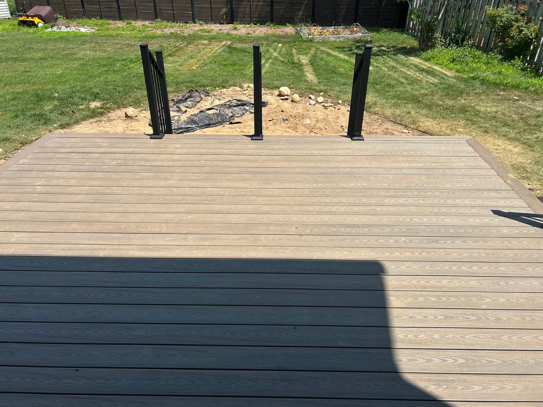 Deck with black railings overlooking a backyard with garden area and grass.