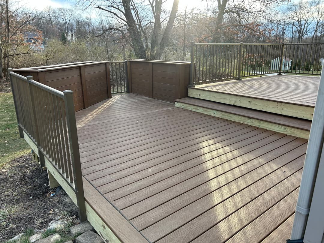 Modern brown composite deck with railings and steps in a wooded backyard setting.