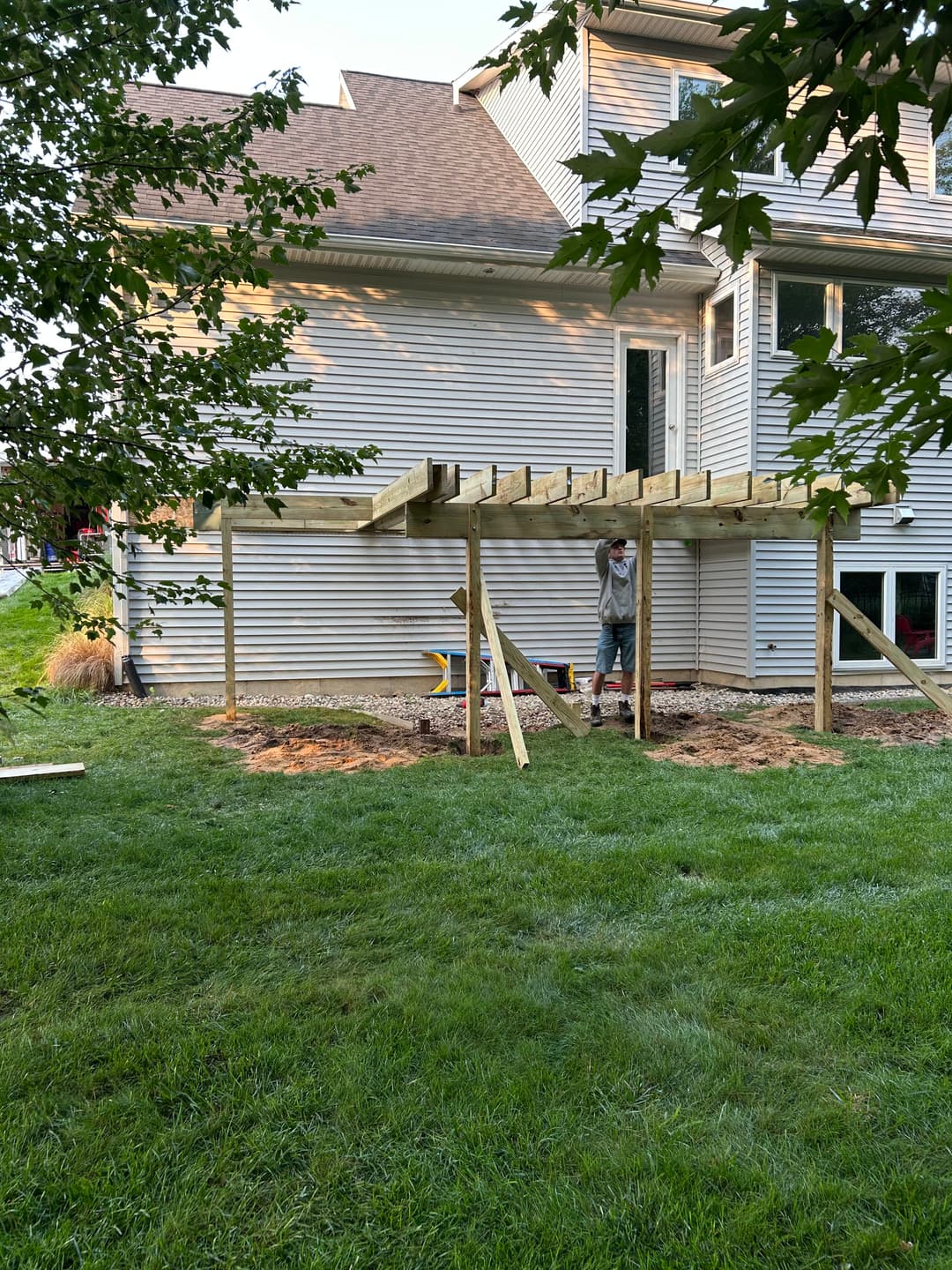 Child constructing a wooden deck framing beside a house on a grassy yard.