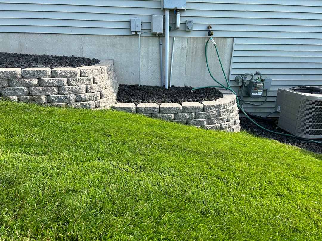 Landscaped backyard with stone retaining wall, black gravel, and green lawn.